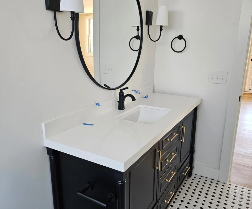 Black vanity with a white top, round mirror and matte black fixtures